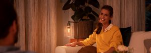 "บรรยากาศห้องนั่งเล่นที่อบอุ่นที่สร้างขึ้นด้วยโคมไฟตั้งโต๊ะ LED ที่ให้ความอบอุ่น หญิงสาวผู้สวมเสื้อสเวตเตอร์สีเหลืองกำลังสนทนาในยามเย็น"